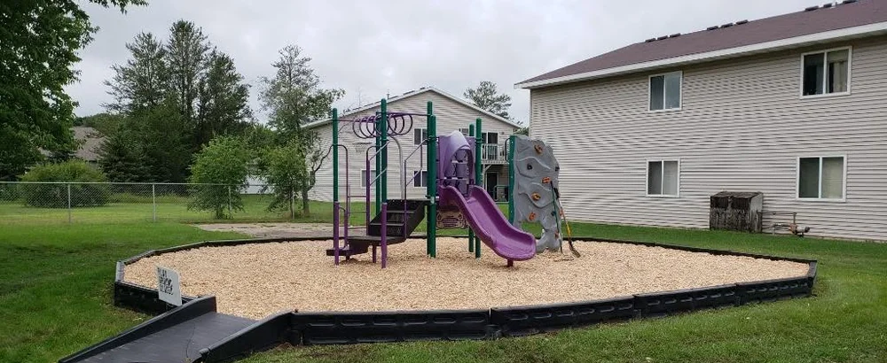 The same playground after, filled with fresh light wood-fibre mulch raked evenly to the border.