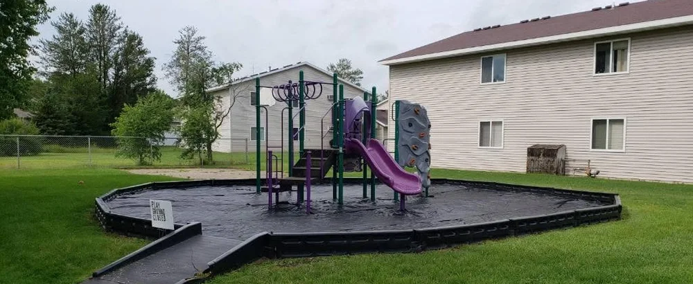 The playground before, with the old surface stripped out and bare liner inside the timber border.